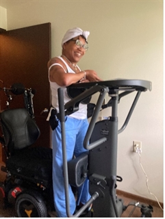 Dalphina smiling and standing with an assistive device