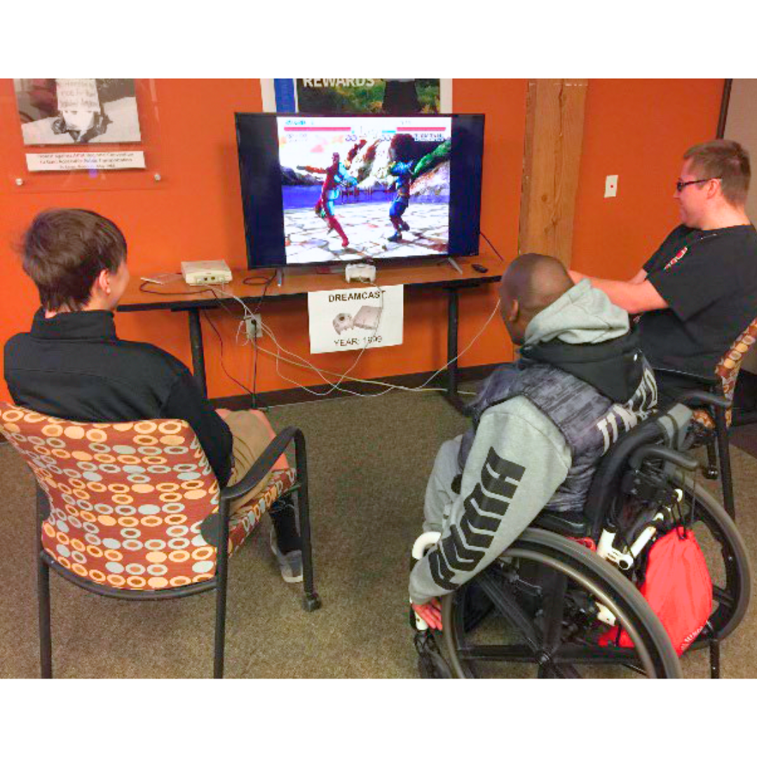 Three people, one in a wheelchair, gathered around a video game