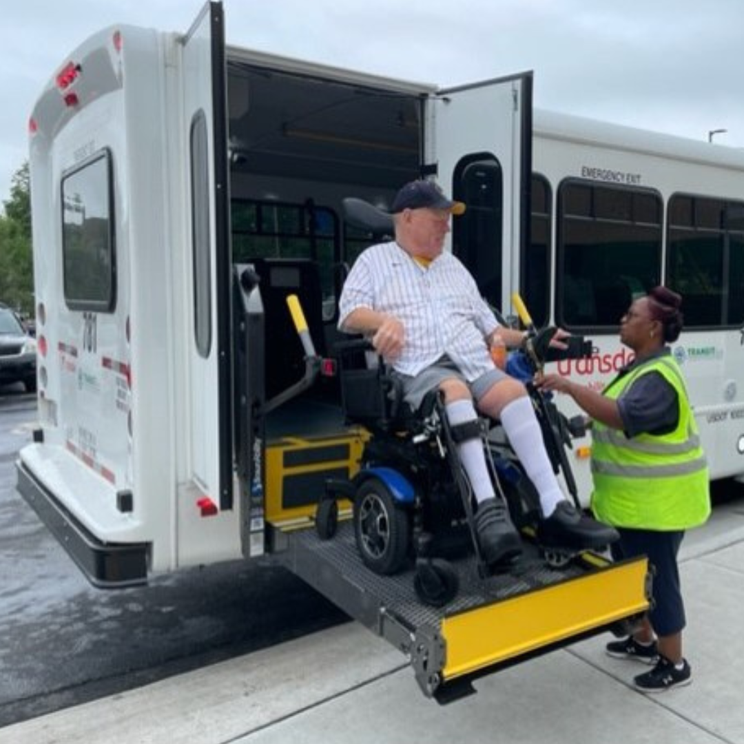 A woman helps a paratransit rider onto a vehicle