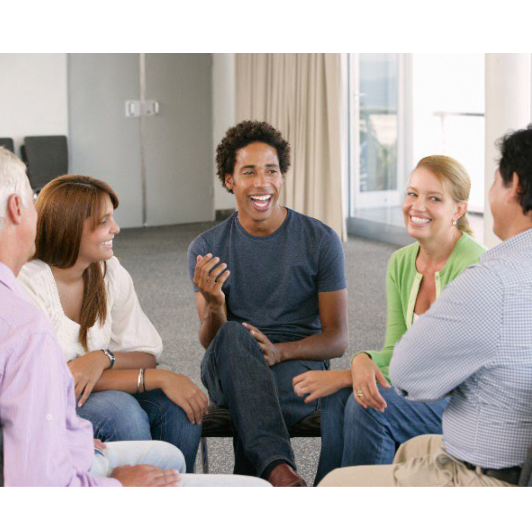 A group of adults sitting in a circle talking and smiling