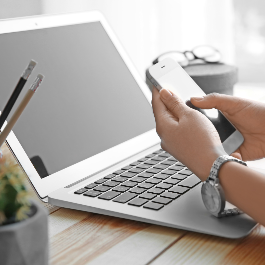 Hands holding a cell phone in front of a laptop